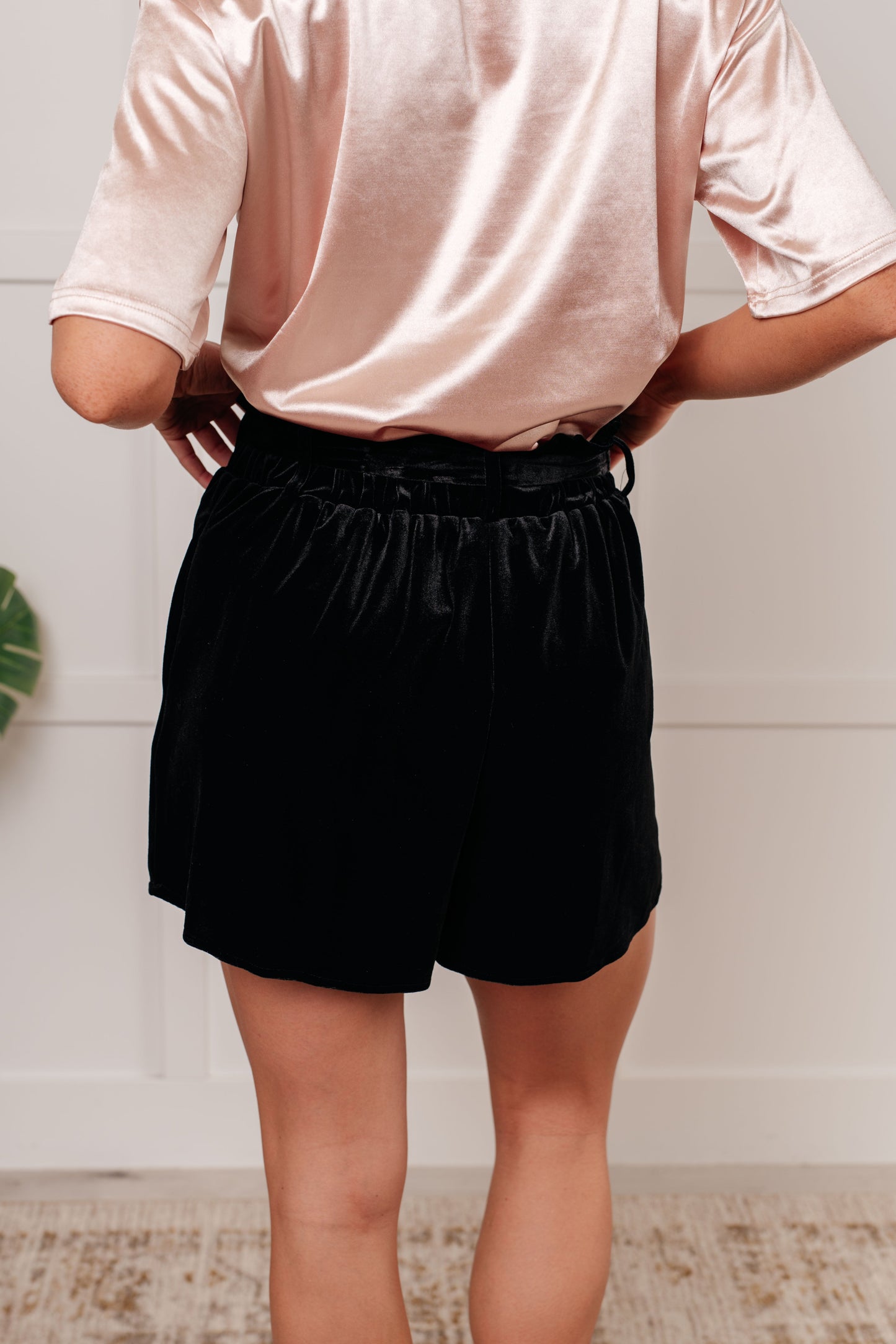 Person wearing a light pink shirt and black shorts against a white wall.