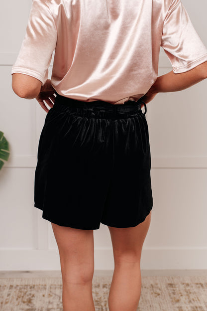 Person wearing a light pink shirt and black shorts against a white wall.