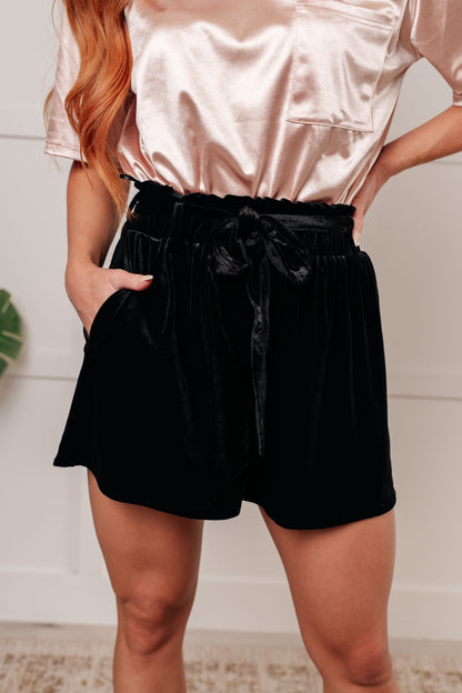Person wearing a satin top and black shorts with a white background