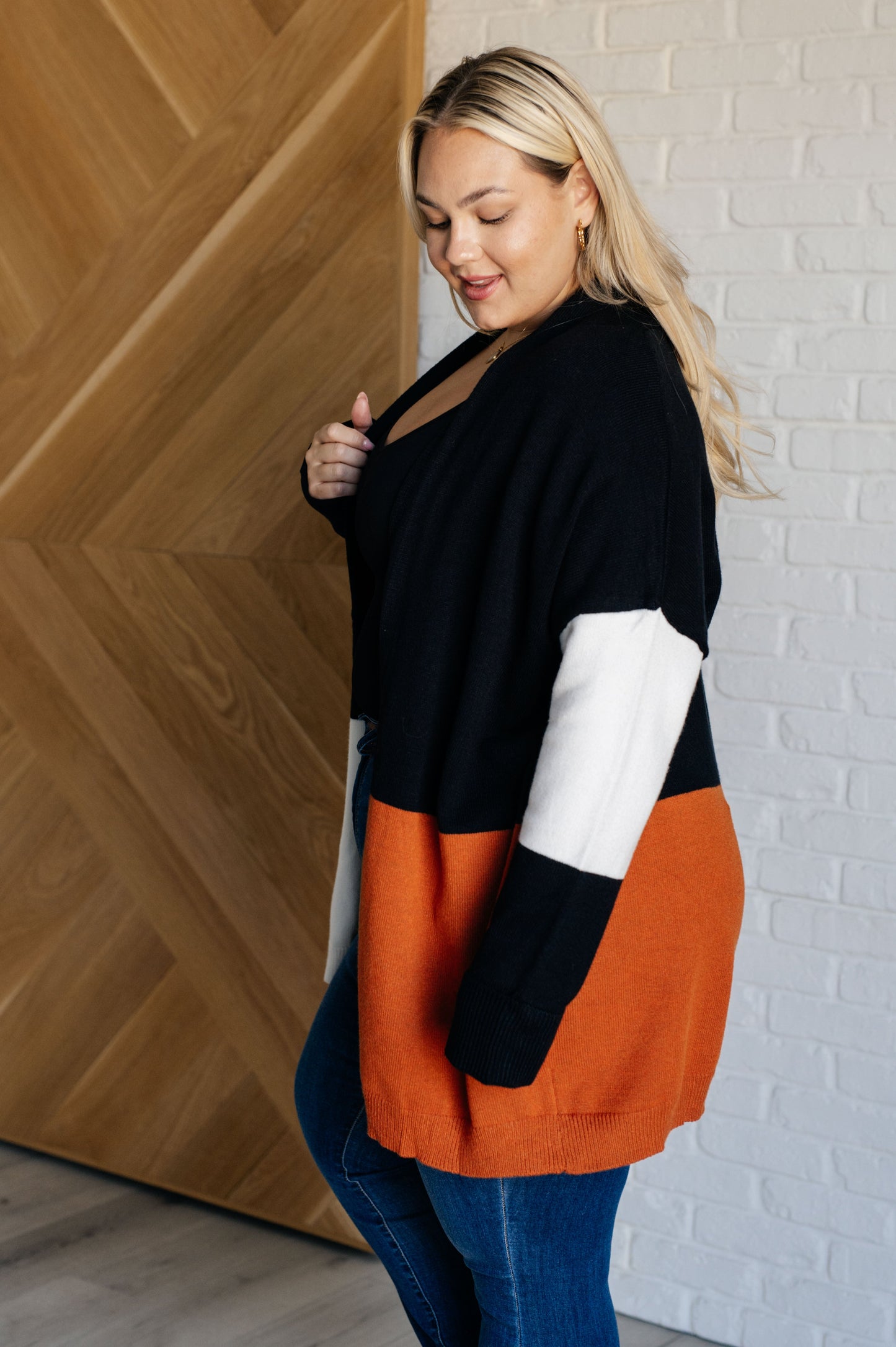 Woman wearing a black, white, and orange color-blocked sweater against a wooden and white brick wall.