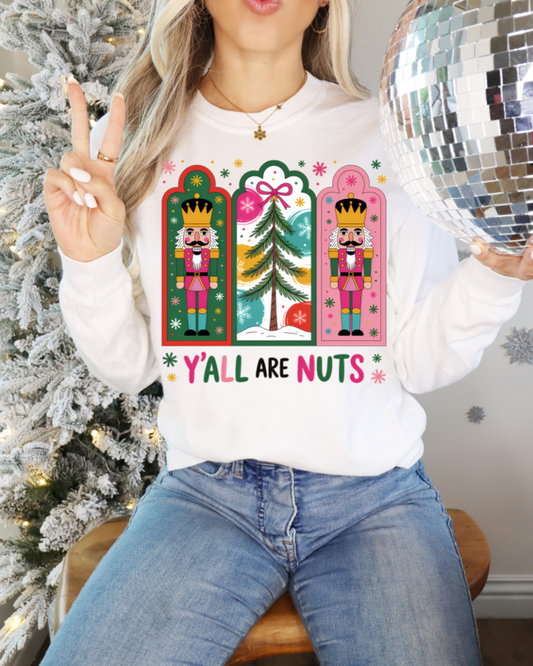 Person wearing a white sweatshirt with Christmas-themed designs and text, sitting in front of a decorated tree.
