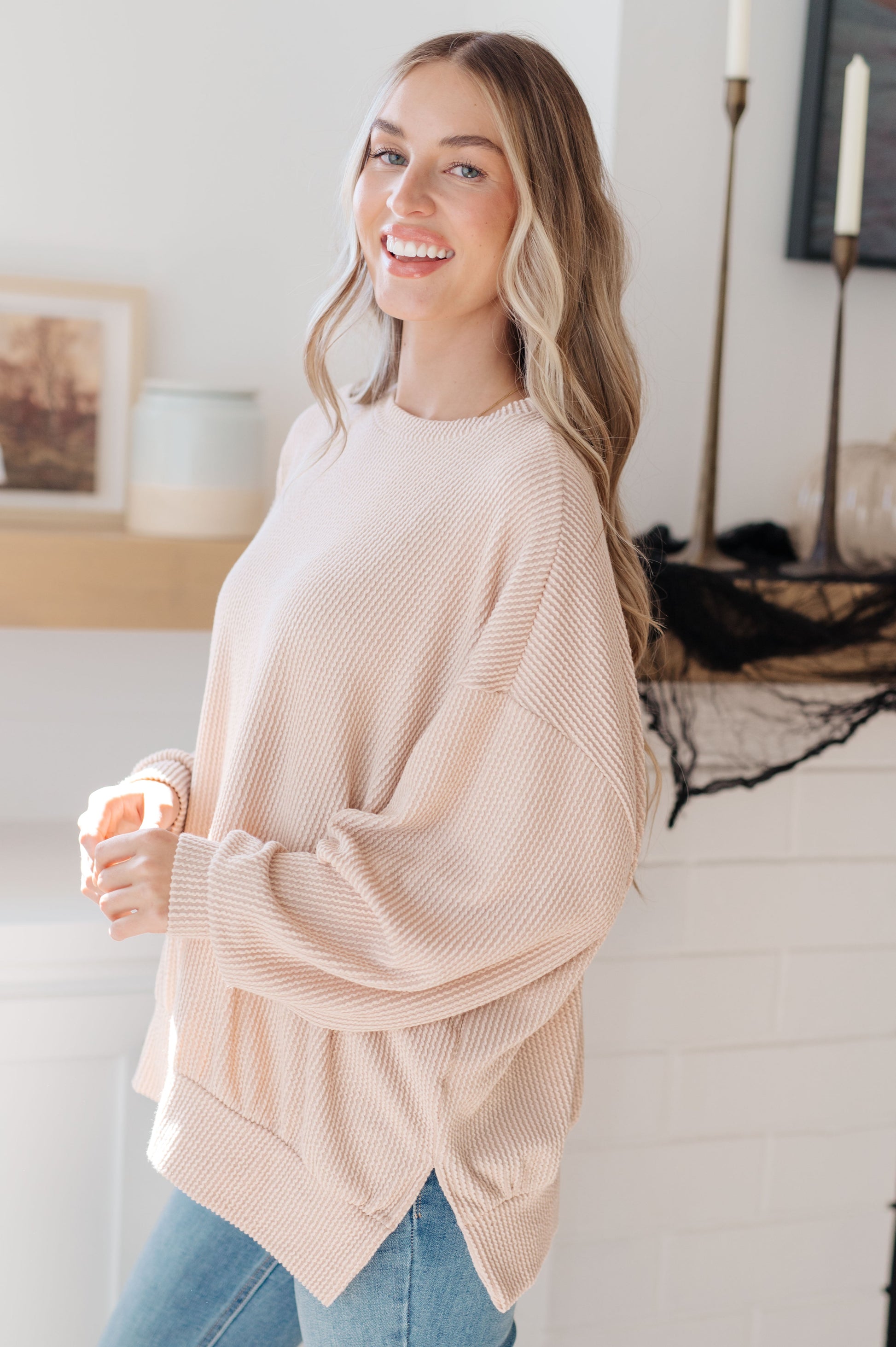 Woman wearing a beige sweater and blue jeans indoors.