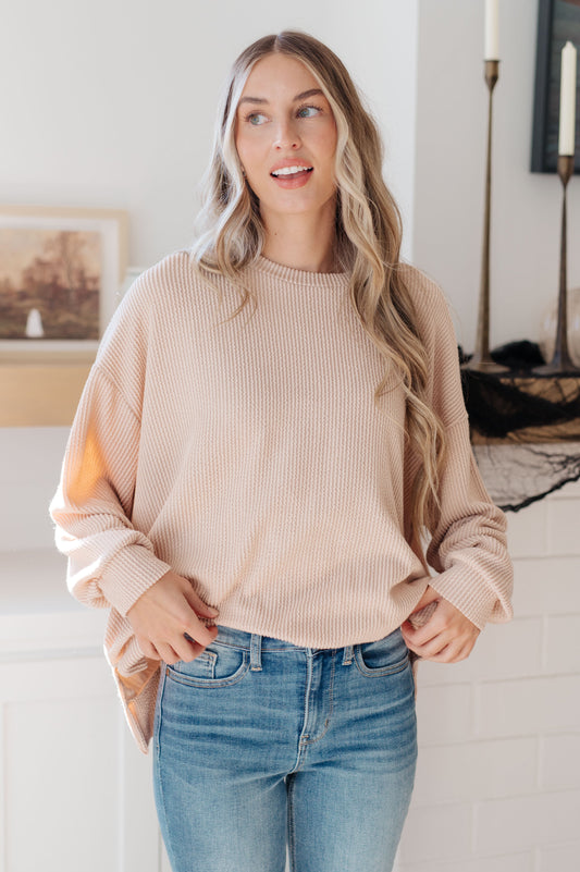 Woman wearing a beige sweater and blue jeans indoors.