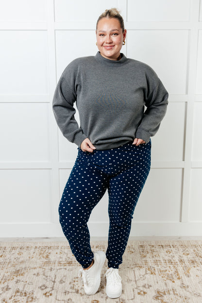Person wearing a gray sweater and navy polka dot pants standing against a white wall.