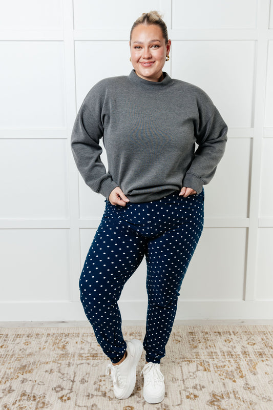 Person wearing a gray sweater and navy polka dot pants standing against a white wall.