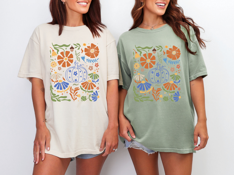Two women wearing t-shirts with floral and pumpkin designs on a plain background
