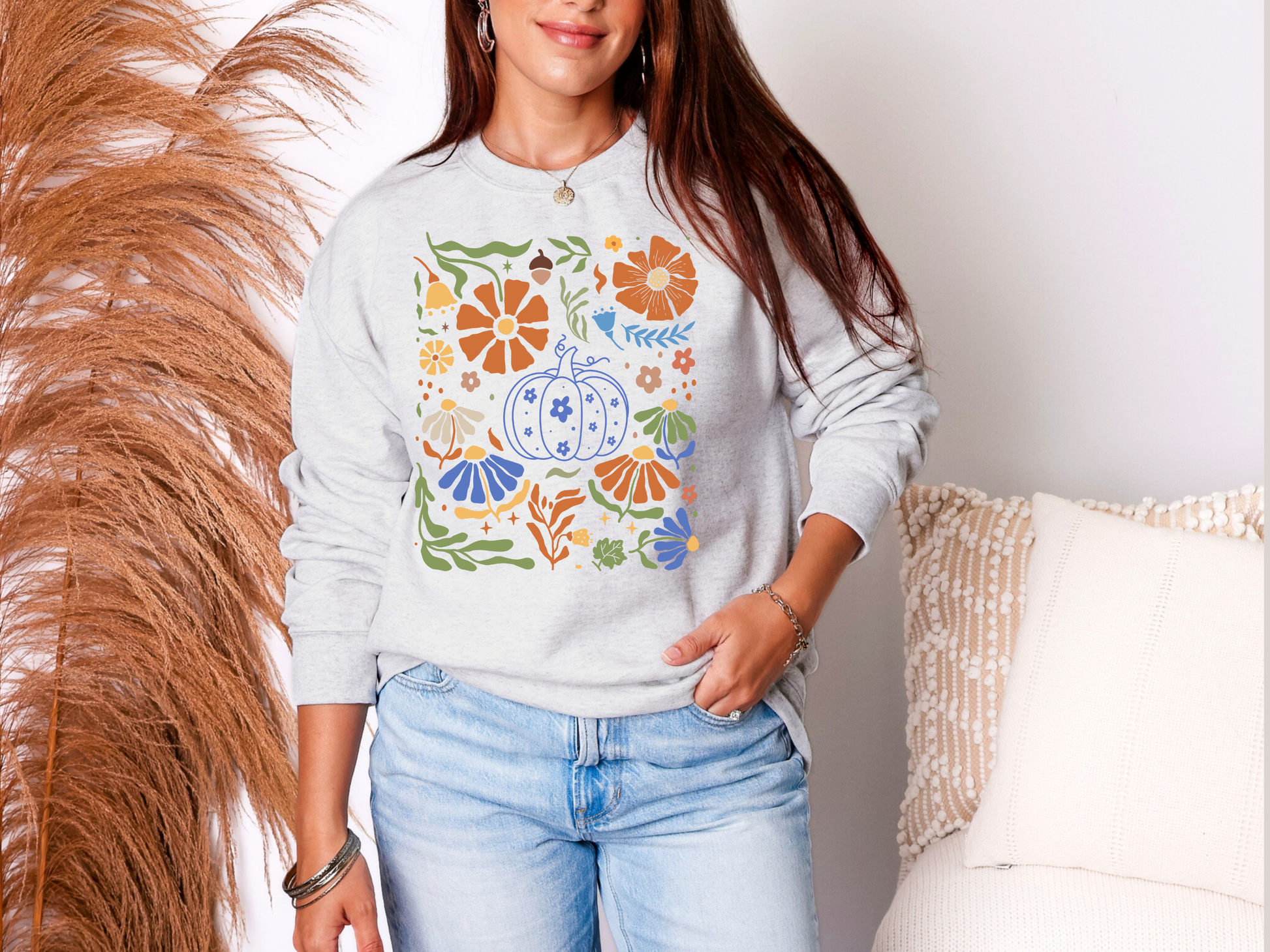 Woman wearing a light gray sweatshirt with a colorful pumpkin design, standing against a neutral background.