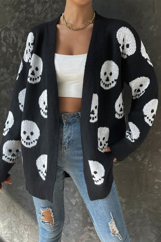 Person wearing a black cardigan with white skull patterns, white top, and ripped jeans.