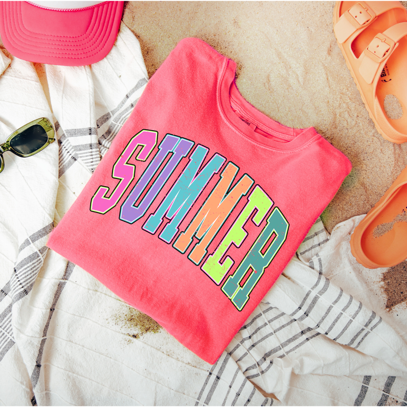 Pink t-shirt with 'SUMMER' in colorful letters on a sandy background