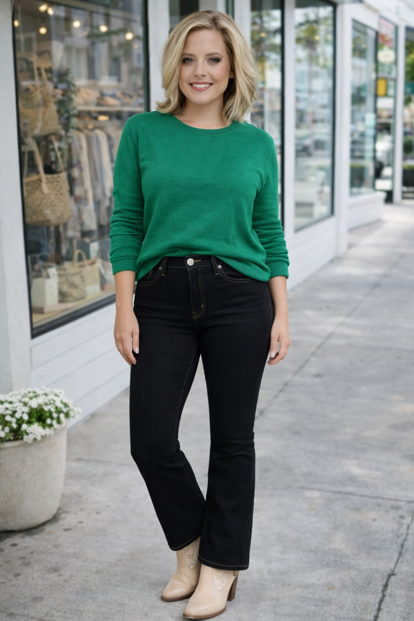 Woman wearing a green sweater and black pants standing on a sidewalk.