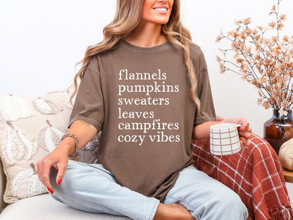 Woman wearing a brown shirt with text, sitting on a couch with a blanket and mug.