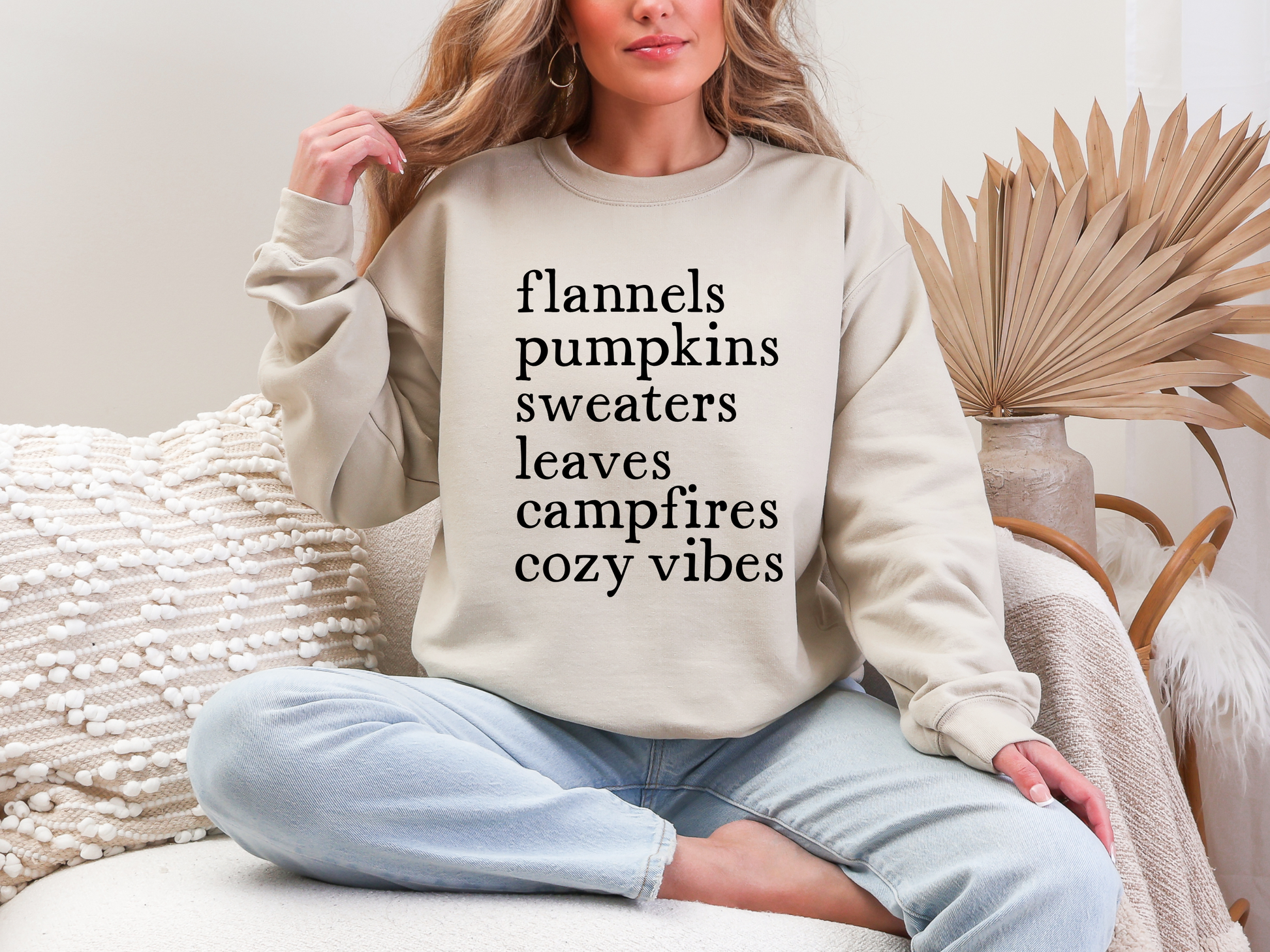 Person wearing a beige sweatshirt with text, sitting in a cozy room.