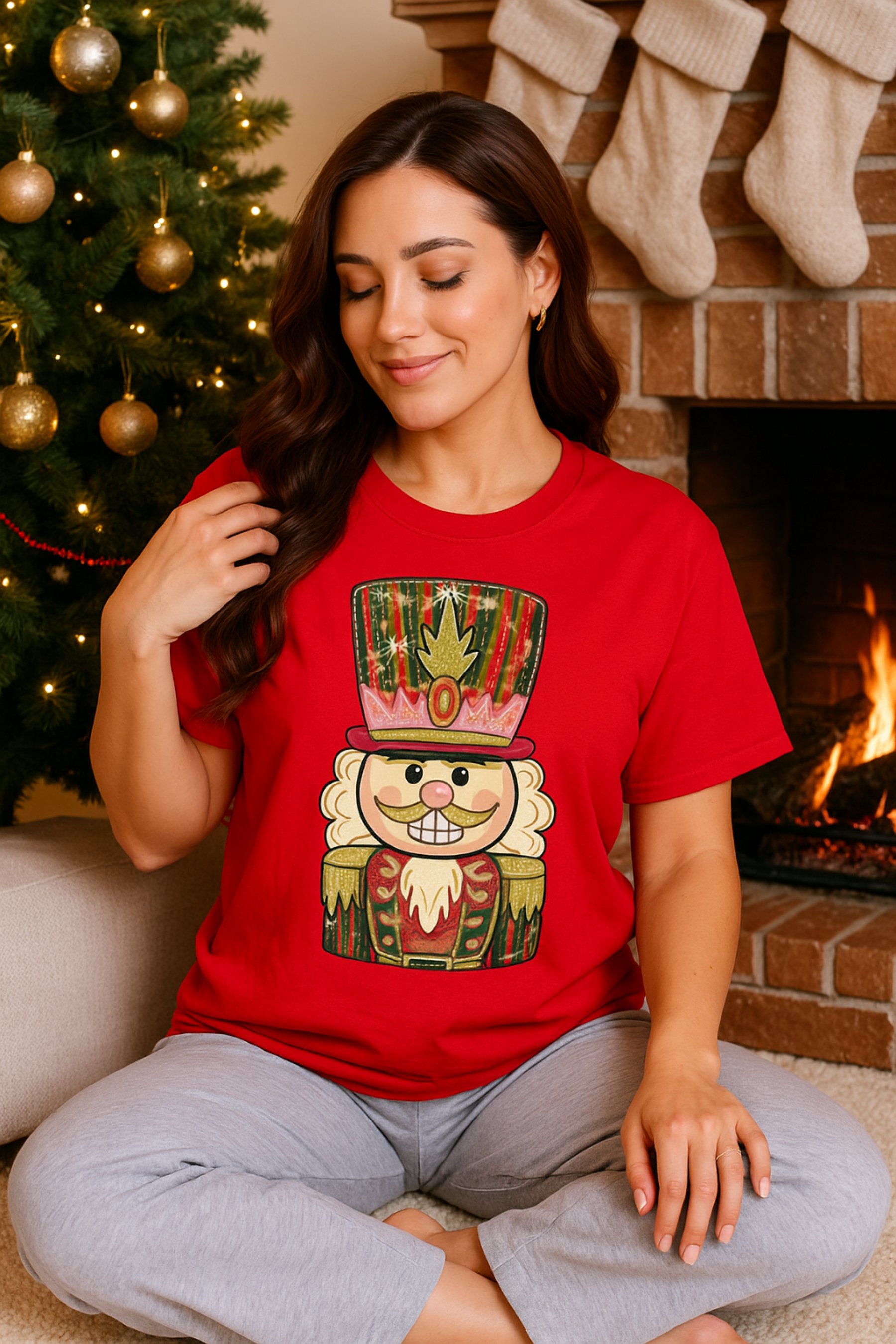 Woman wearing a red t-shirt with a nutcracker design in front of a Christmas tree and fireplace.