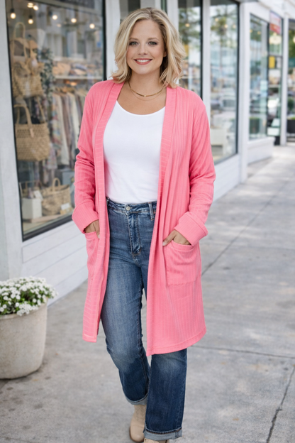 Woman wearing a pink cardigan, white top, and blue jeans on a sidewalk.
