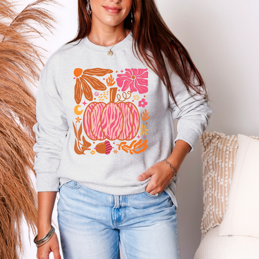 Person wearing a light gray sweatshirt with a colorful pumpkin design, standing against a neutral background.