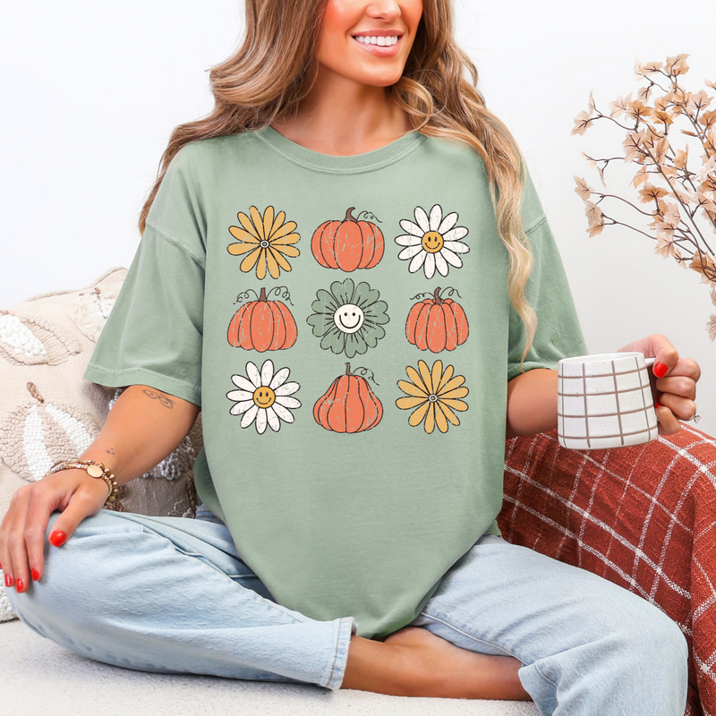 Woman wearing a green t-shirt with pumpkins and flowers, sitting on a couch holding a mug.