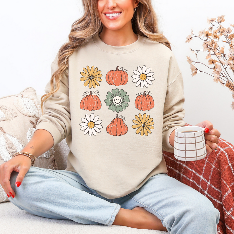 Woman wearing a beige sweatshirt with autumn-themed designs, sitting on a couch holding a mug.