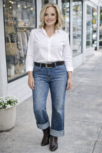 Woman wearing a white shirt, blue jeans, and black boots standing on a sidewalk.