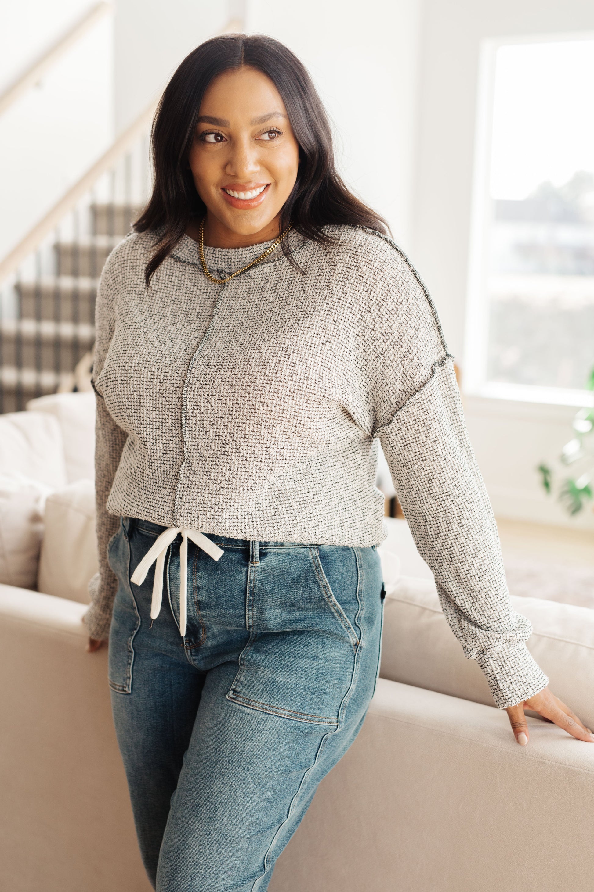 Woman wearing a gray sweater and blue jeans in a living room.