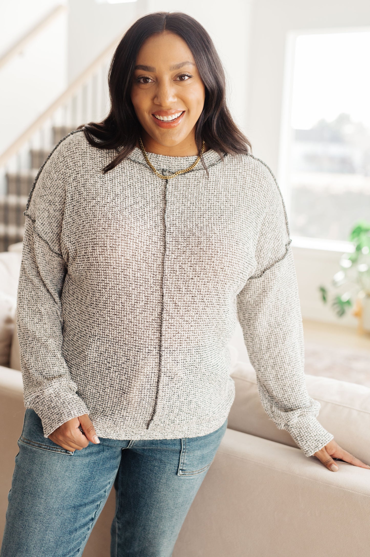 Woman wearing a gray sweater and blue jeans standing in a living room.
