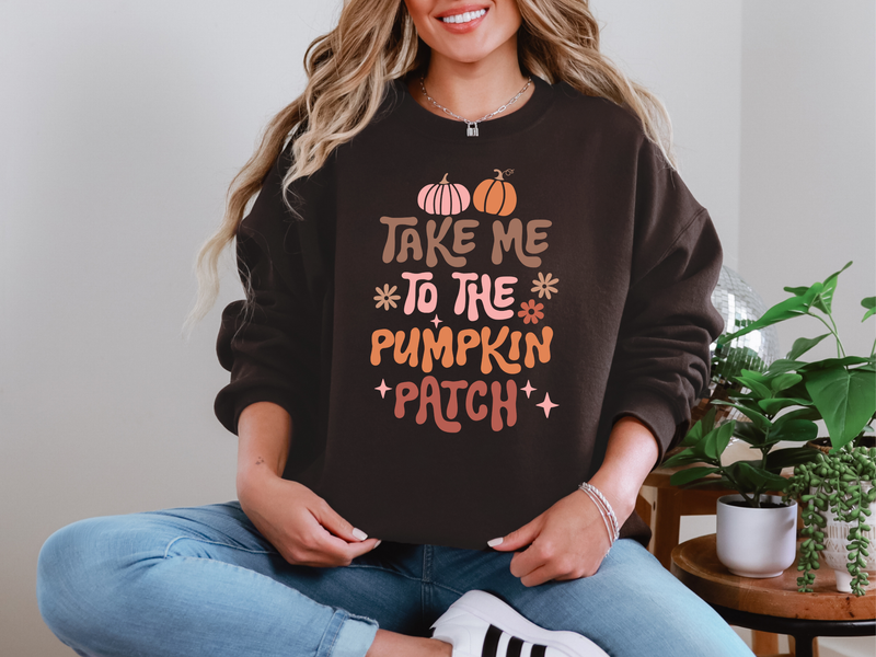 Woman wearing a black sweatshirt with 'Take Me to the Pumpkin Patch' text and graphics, sitting indoors.
