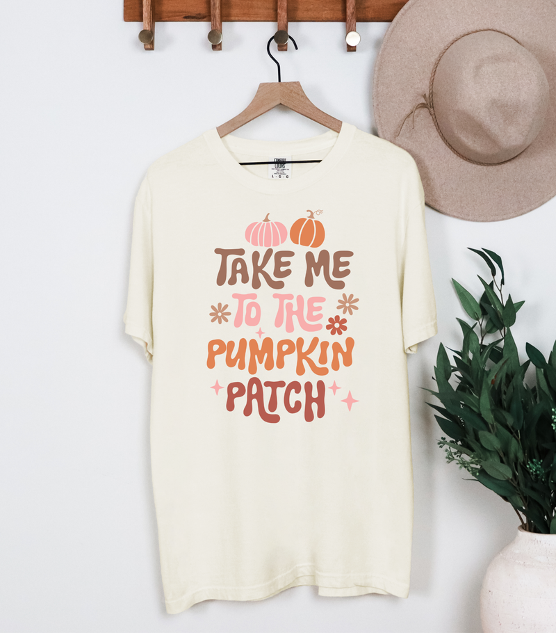 White t-shirt with 'Take Me to the Pumpkin Patch' text on a hanger against a white wall.
