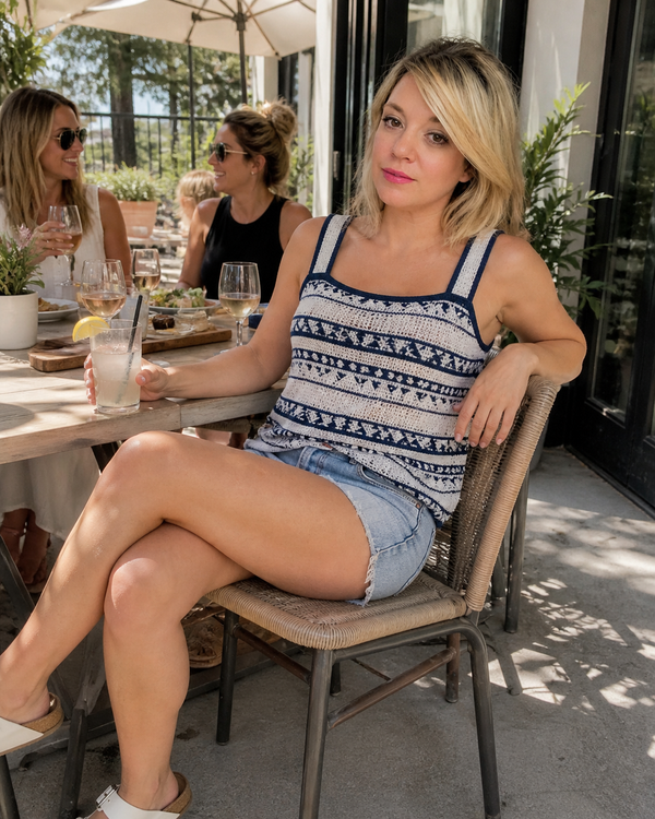 Woman sitting at an outdoor dining table with friends, wearing a patterned top and denim shorts.