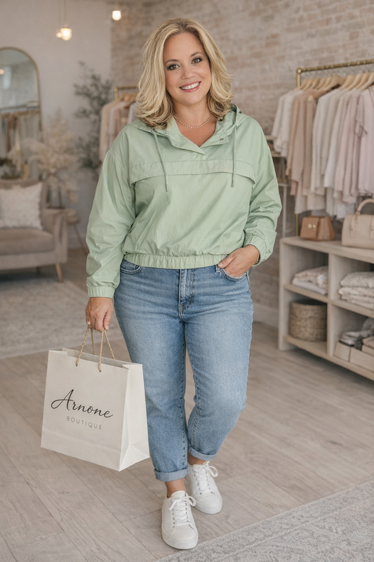Woman in a light green jacket and blue jeans holding a shopping bag in a store.