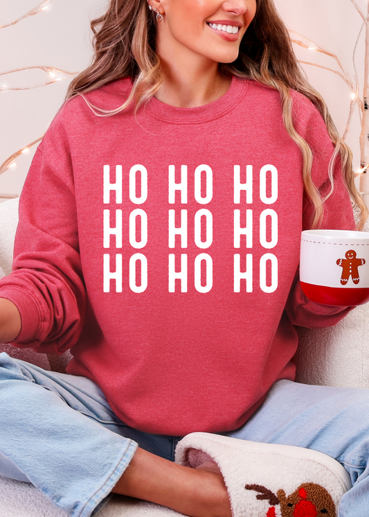 Person wearing a red sweater with 'HO HO HO' text, holding a mug, sitting on a couch with decorative lights in the background.